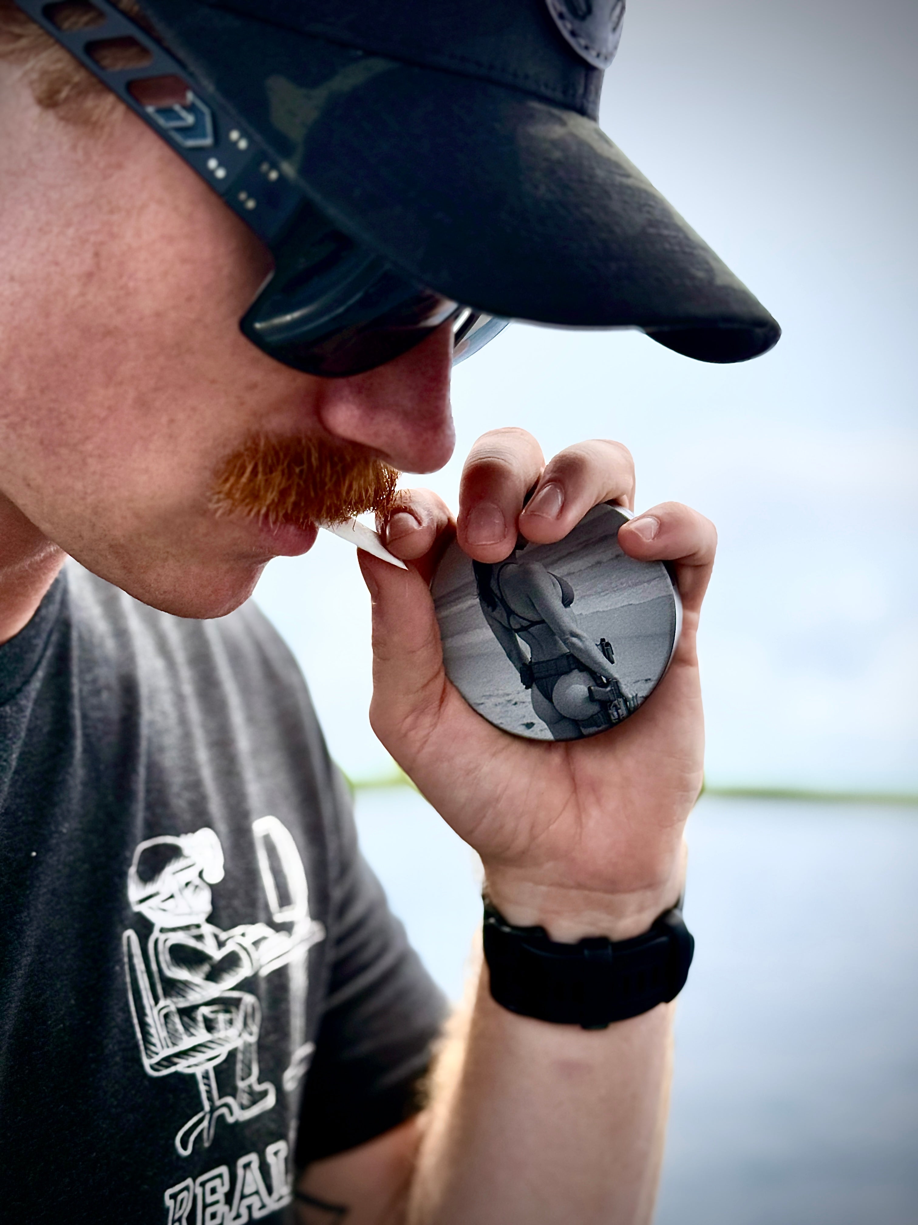 Metal Zyn Can for nicotine pouches with engraved design of "pin-up" style woman in a. bikini and tactical gear. With integrated bottle opener. shown being used by military style man.